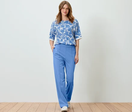 Frau posiert in hellblauem, bedrucktem Sweatshirt und blauer Hose.