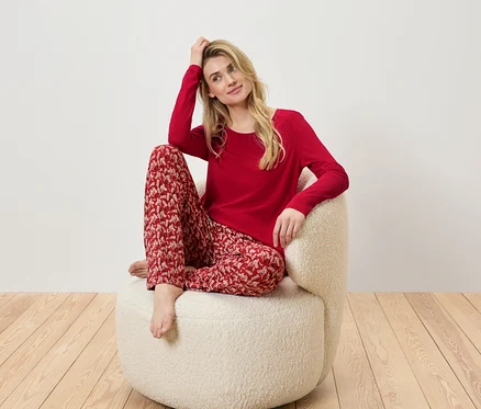 Blonde Frau sitzt in einem Sessel und trägt einen roten Pyjama mit Muster.