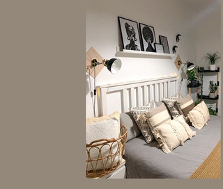 Schlafzimmer mit Bett, Kissen und einem schwarzen Blumenregal mit 4 Ablagen.