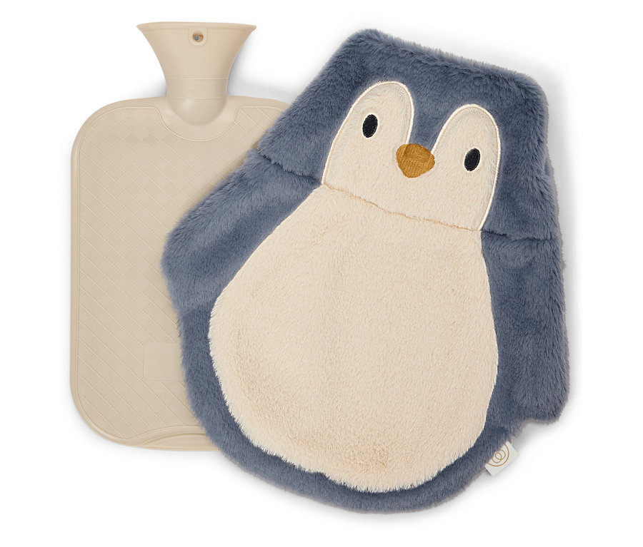 Eine beige Wärmflasche liegt neben einer flauschigen Wärmflaschenhülle in Pinguinform.