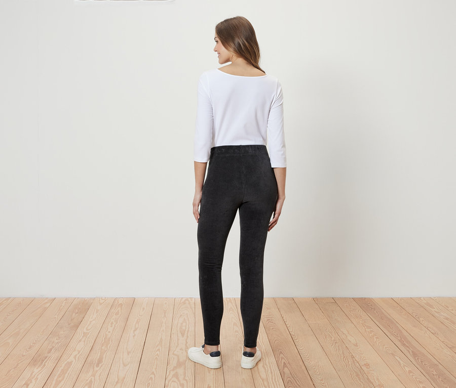 Eine Frau steht mit dem Rücken zur Kamera und trägt ein weißes Dreiviertelarmshirt und graue Leggings.