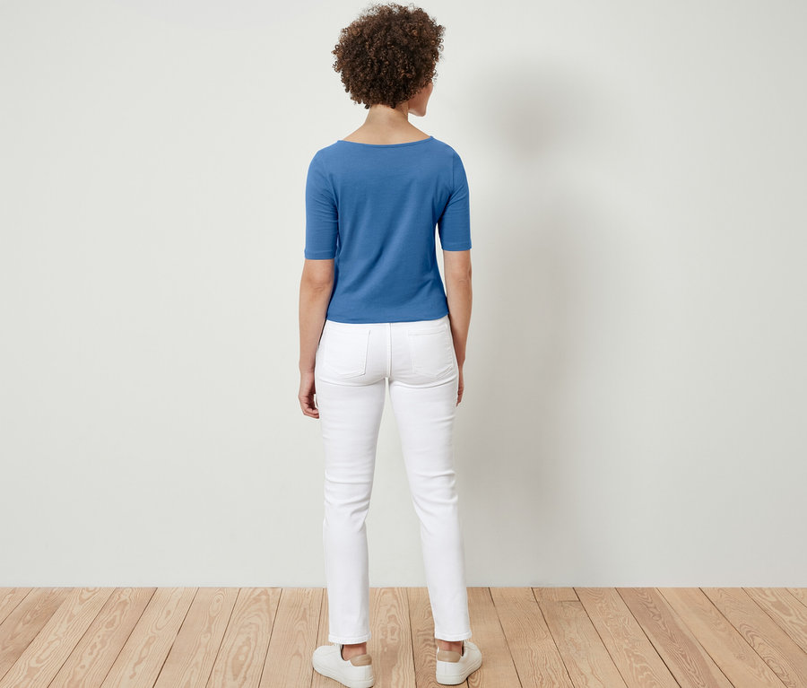 Eine Frau steht mit dem Rücken zur Kamera und trägt ein blaues Halbarmshirt.