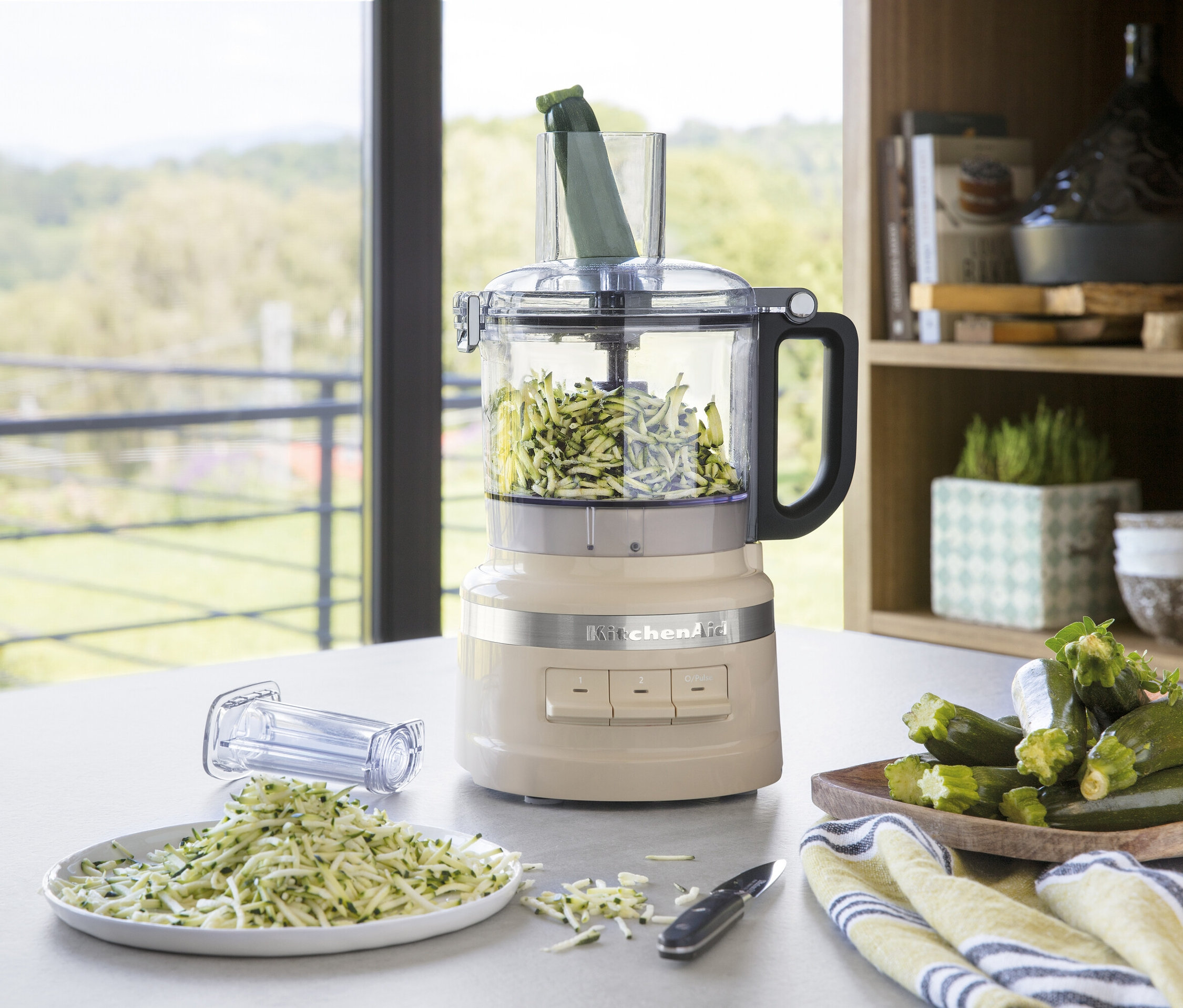 Eine cremefarbene KitchenAid Küchenmaschine verarbeitet Zucchini zu Julienne-Streifen, die auf einem Teller liegen.