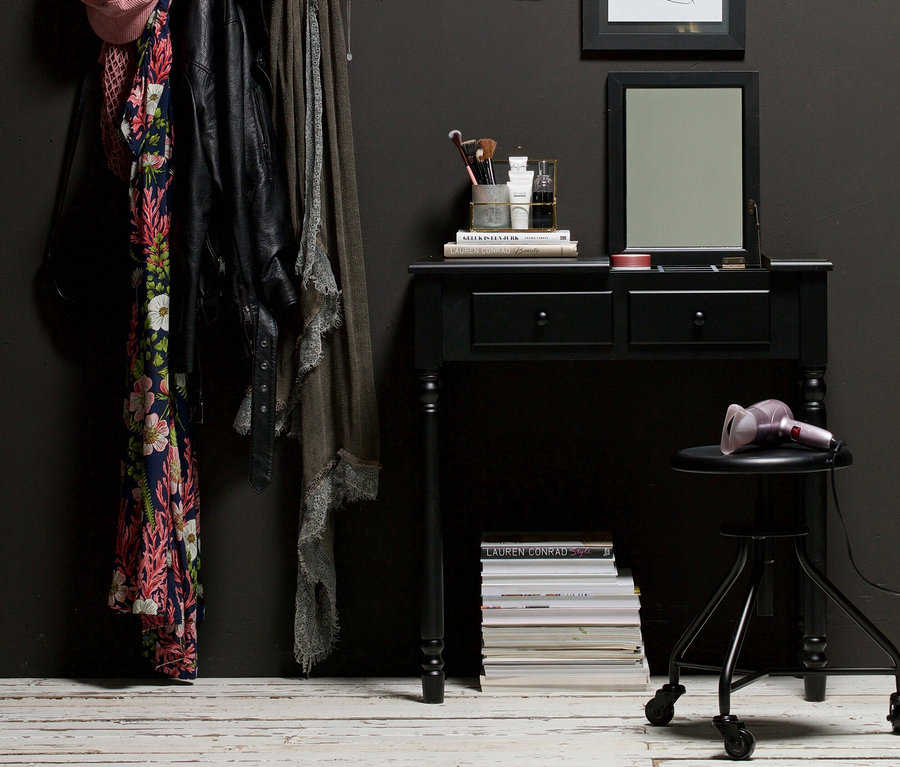 Schwarzer Woood Romy Frisiertisch mit Zubehör und Kleiderständer mit Kleidung an dunkelgrauer Wand.