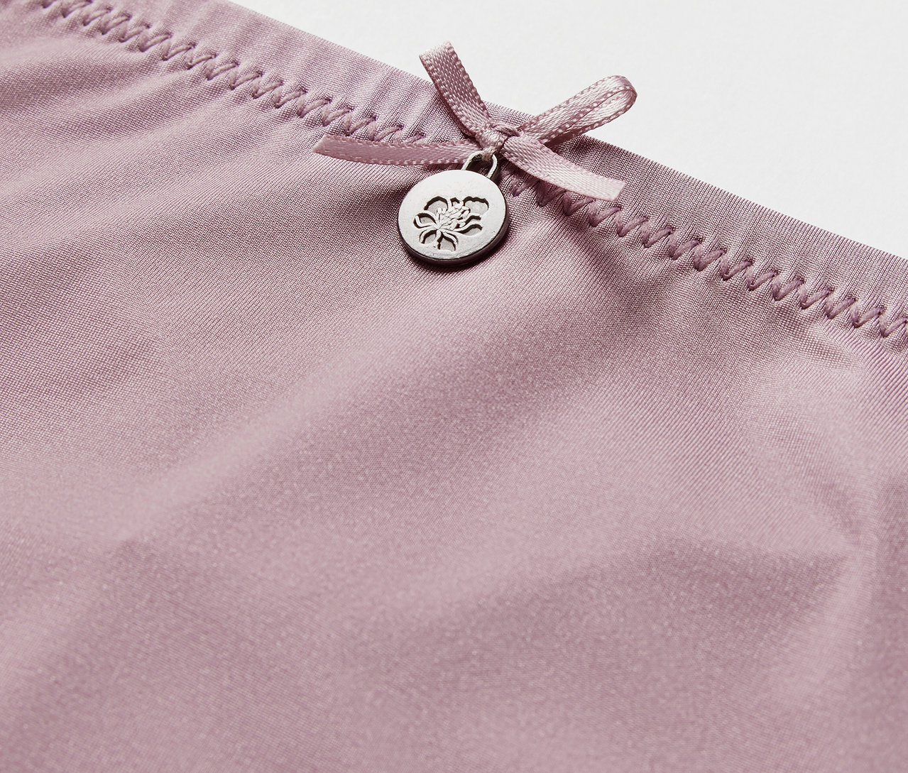 Detailaufnahme eines lila Strings mit Schleife und Anhänger.