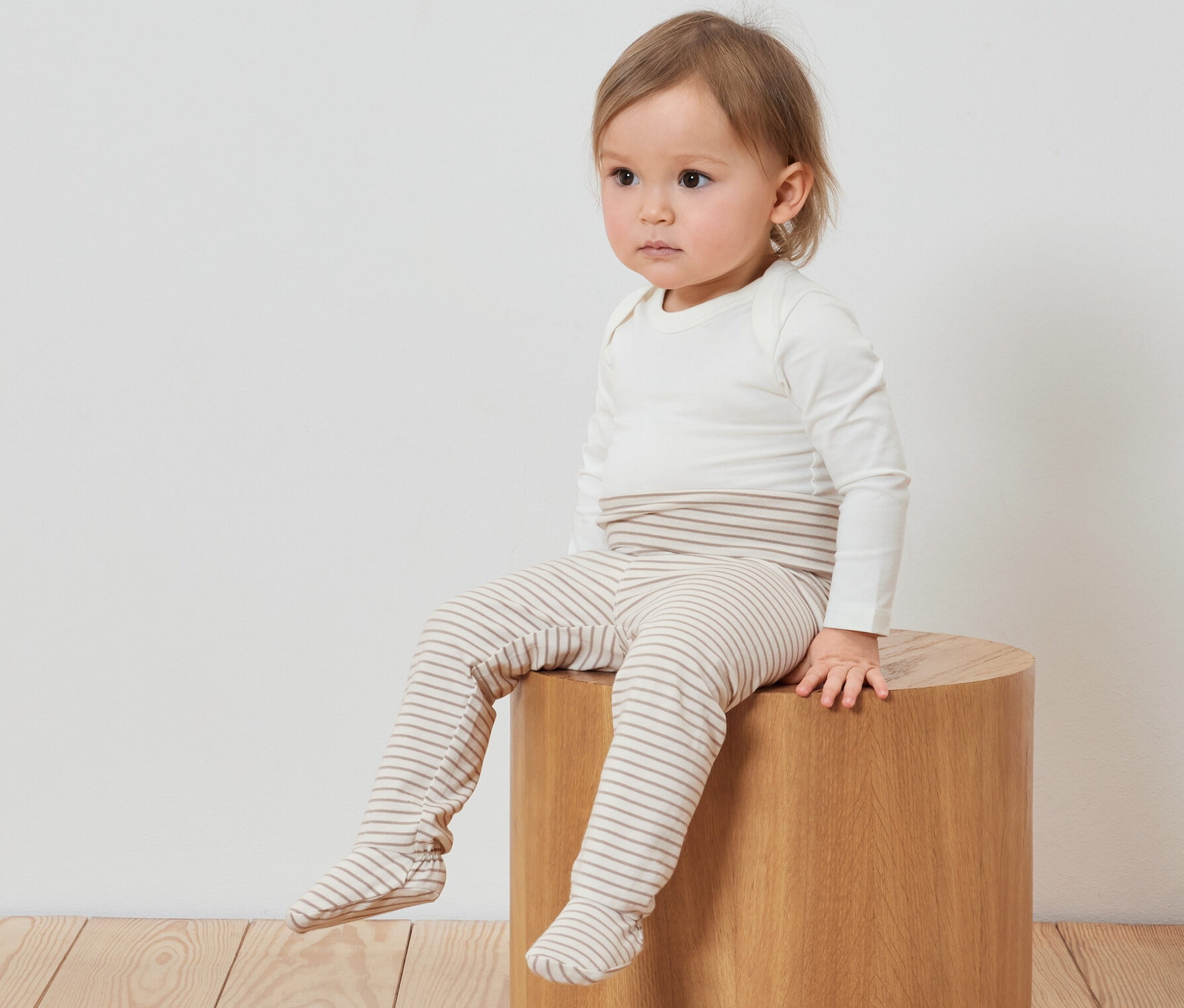 Ein Kind sitzt auf einem Holzhocker und trägt 3 Baby-Strampelhosen.