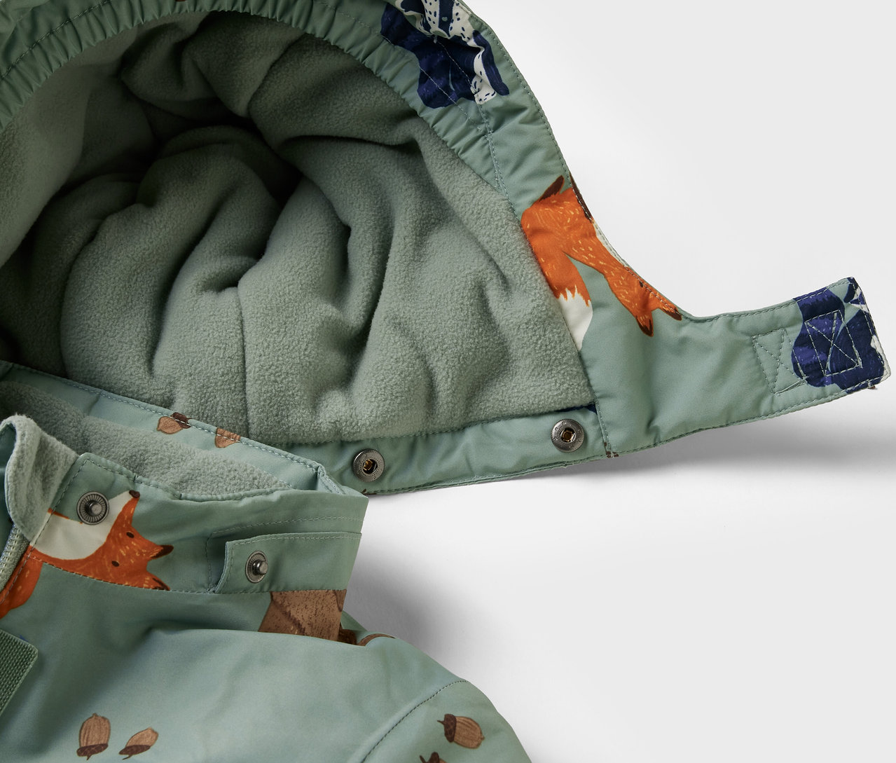 Detailansicht eines Kinder-Schneeanzugs mit Kapuze und Fuchs- und Eichelmuster.