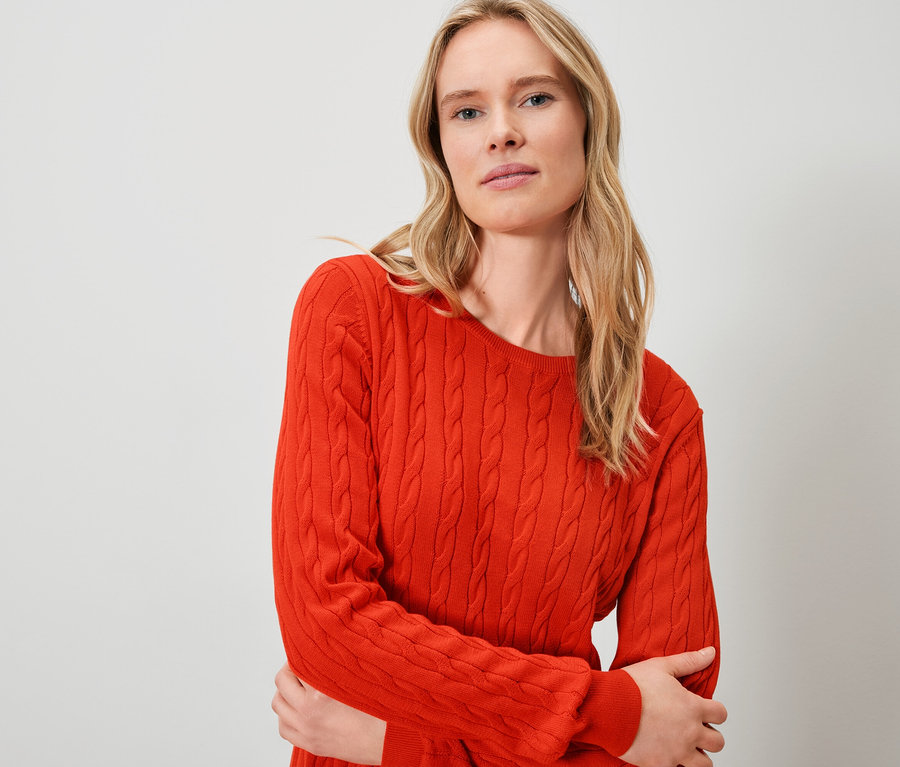 Blonde Frau trägt einen orangefarbenen Pullover.