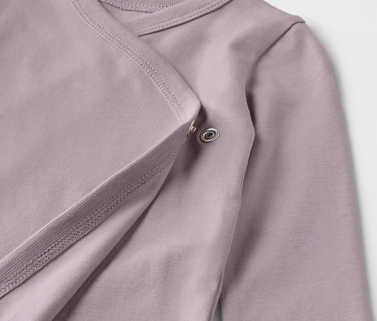 Detailansicht eines lila Baby-Bodys mit langen Ärmeln und Mitwachsfunktion.