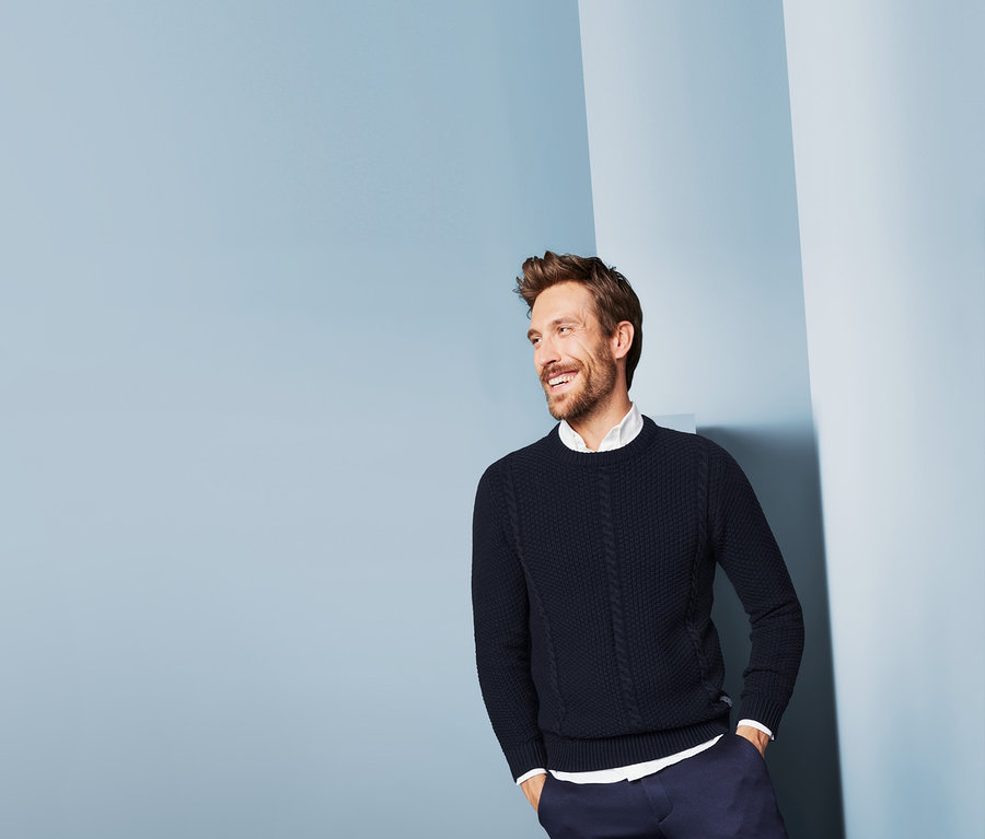 Mann mit braunen Haaren und Bart im Strickpullover.