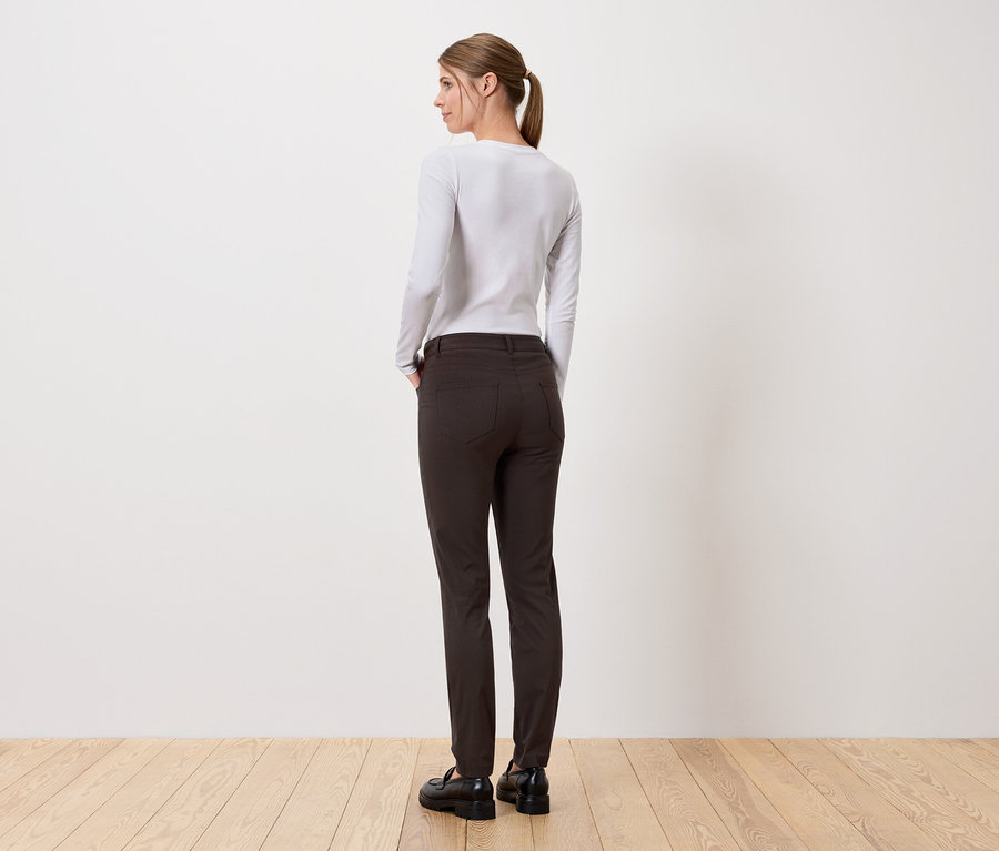 Eine Frau steht mit dem Rücken zur Kamera und trägt eine lange Hose und ein langärmeliges Oberteil.