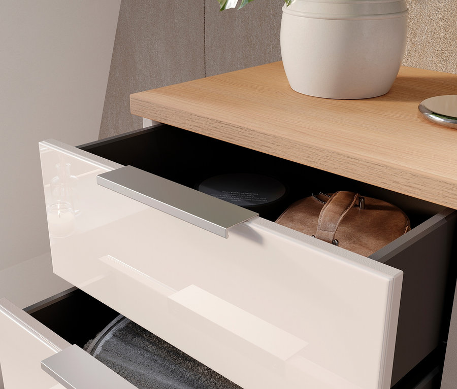 Detailansicht eines teilweise geöffneten Nachttischschranks mit hellbeige glänzenden Schubladen, einer braunen Tasche und einer grauen Decke.