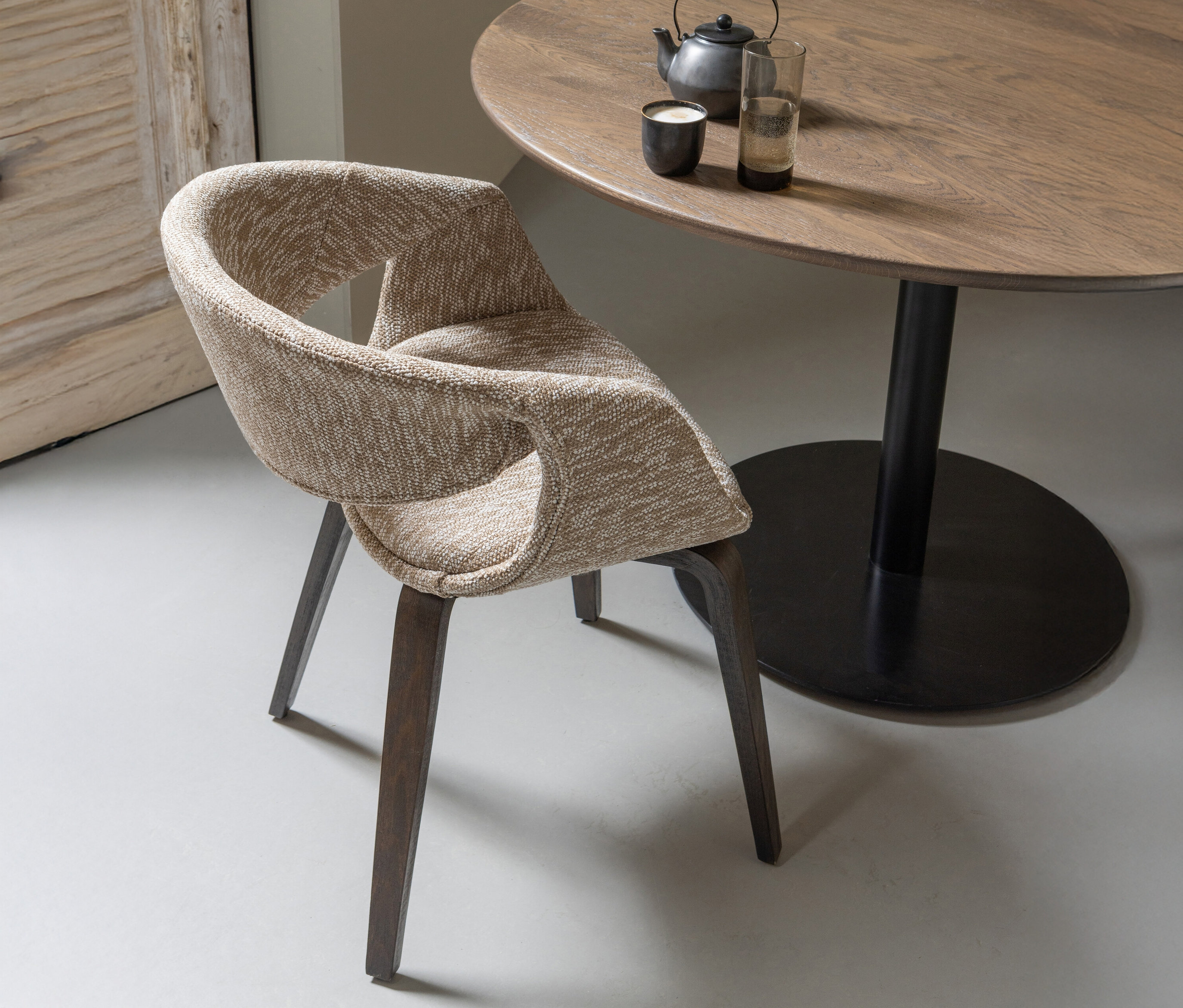 Sandfarbener WOOOD Esszimmerstuhl »Yossi« mit Holzfuß aus einem 2er-Set steht an einem Holztisch mit Teekanne und Glas.