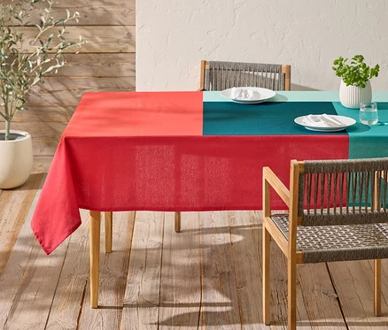 Ein Tisch mit einer rot und blaugrün karierten Tischdecke und zwei Stühlen steht auf einer Holzterrasse.