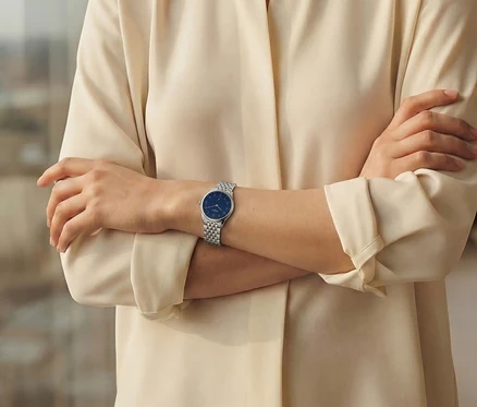 Eine Frau mit verschränkten Armen trägt eine silberne Armbanduhr mit blauem Zifferblatt.