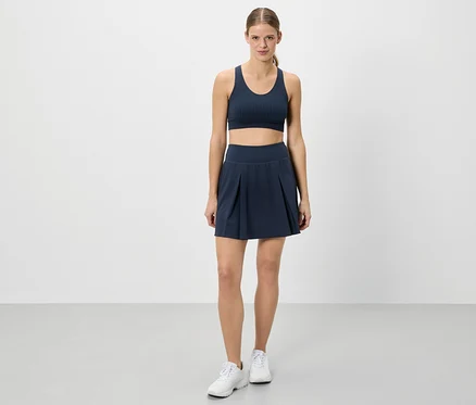 Eine Frau steht in Sportbekleidung vor einem weißen Hintergrund.