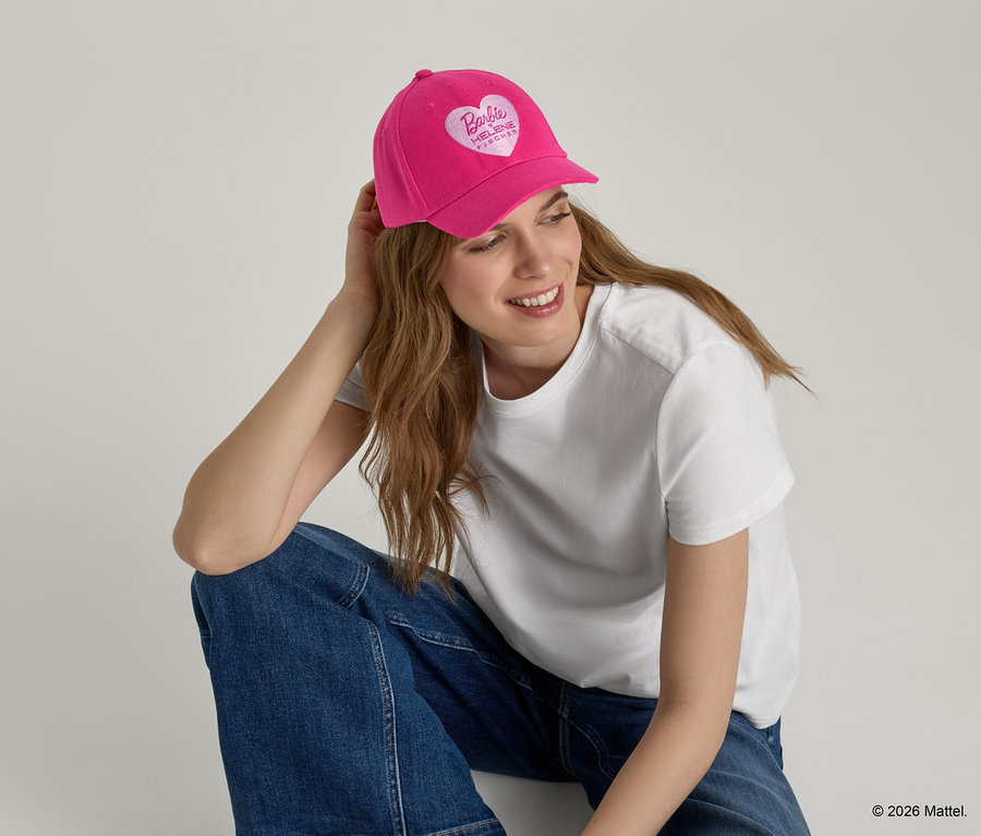 Frau mit pinker Baseballkappe mit Herzlogo, weißem T-Shirt und Jeans.