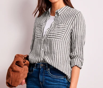 Frau trägt eine dunkelbraun-weiß gestreifte Street One Hemdbluse über einem weißen T-Shirt, blaue Jeans und hält eine braune Clutch.