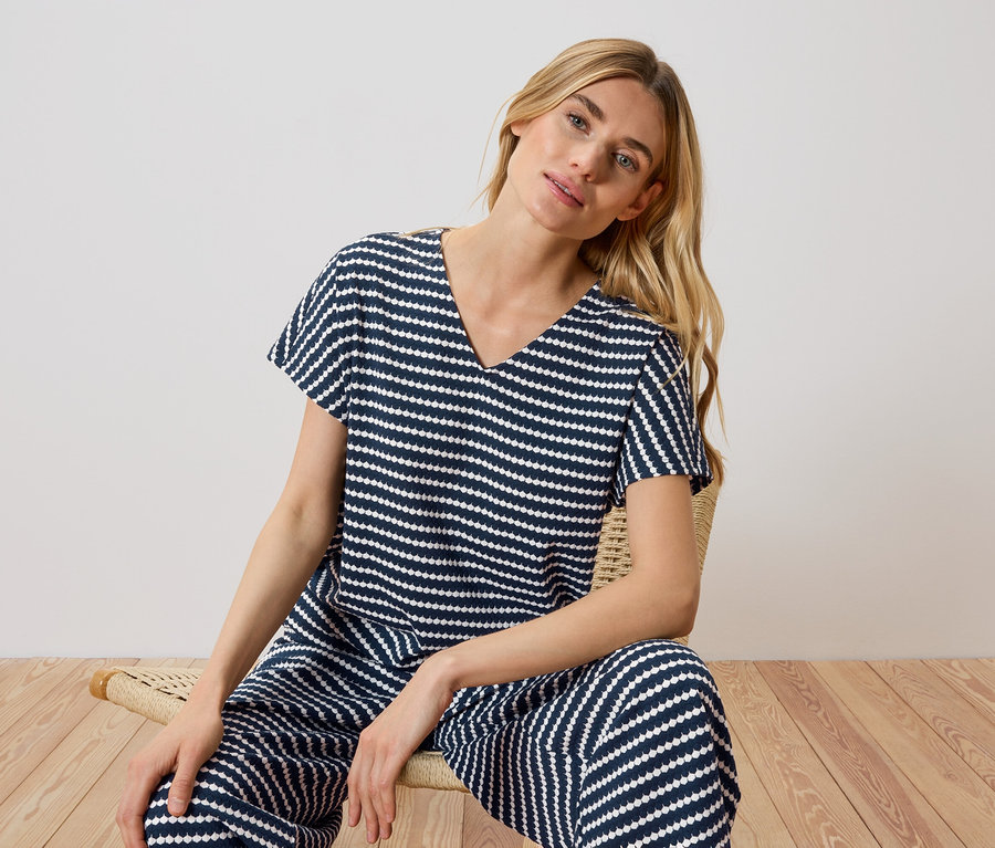 Blonde Frau sitzt auf einem Stuhl und trägt einen marineblau-weiß gestreiften Pyjama.