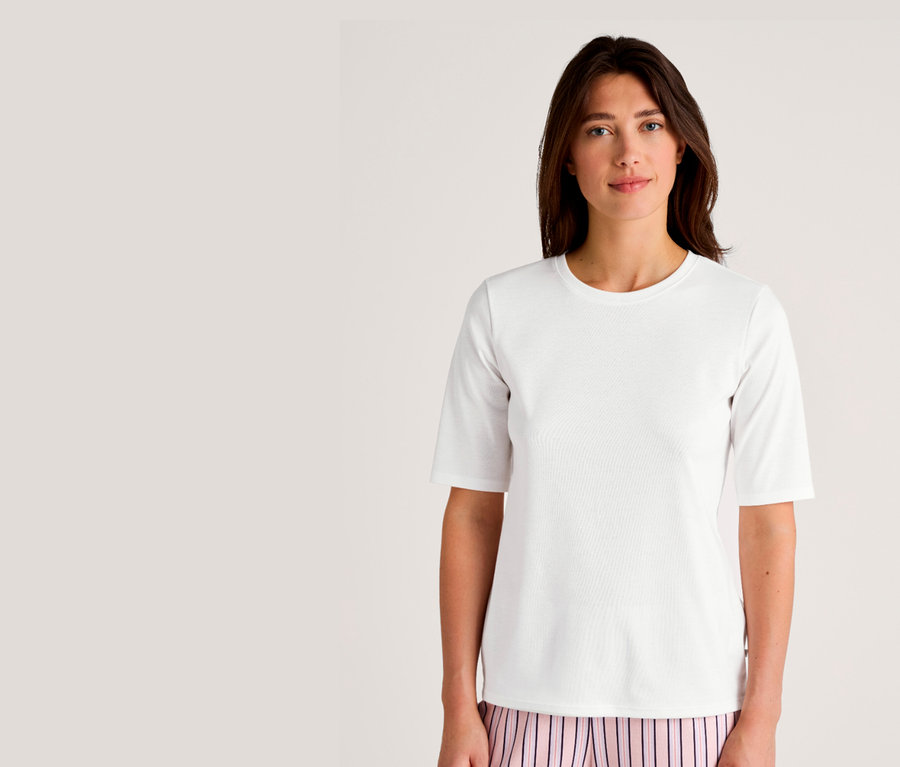 Frau trägt ein weißes T-Shirt mit kurzen Ärmeln und eine rosa-gestreifte Hose.