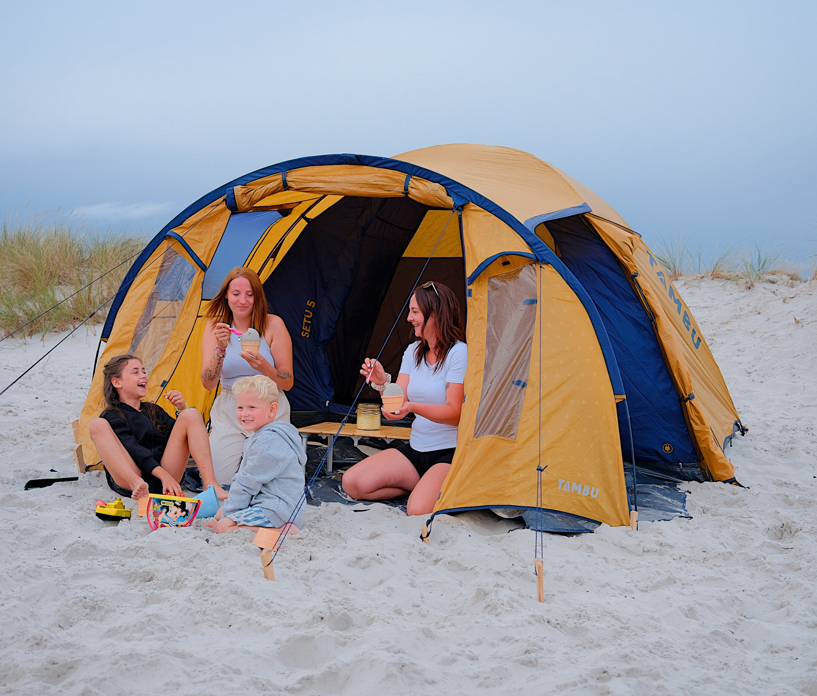 Vier Personen sitzen vor dem Tambu »SETU 5« 5-Personen-Kuppelzelt am Strand und essen Eis.