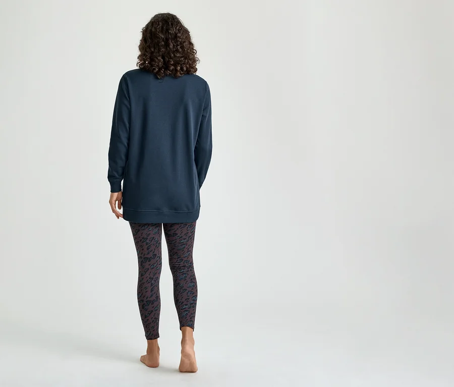 Eine Frau von hinten, die ein dunkelblaues Langarmshirt und dunkle gemusterte Leggings trägt und barfuß steht.