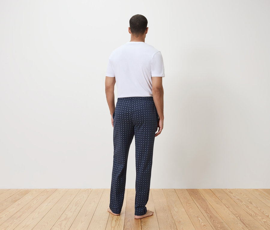 Mann von hinten in einem weißen T-Shirt und einer marineblauen Schlafanzughose mit geometrischem Muster.