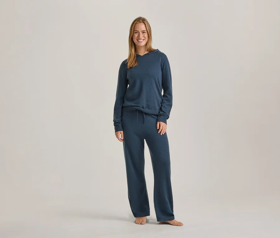Lächelnde Frau steht in blauem Langarm-Hoodie und passender weiter Hose.