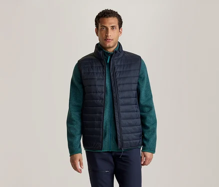 Ein Mann steht frontal da und trägt eine dunkelblaue Steppweste über einer grünen Fleecejacke und einer dunkelblauen Hose.