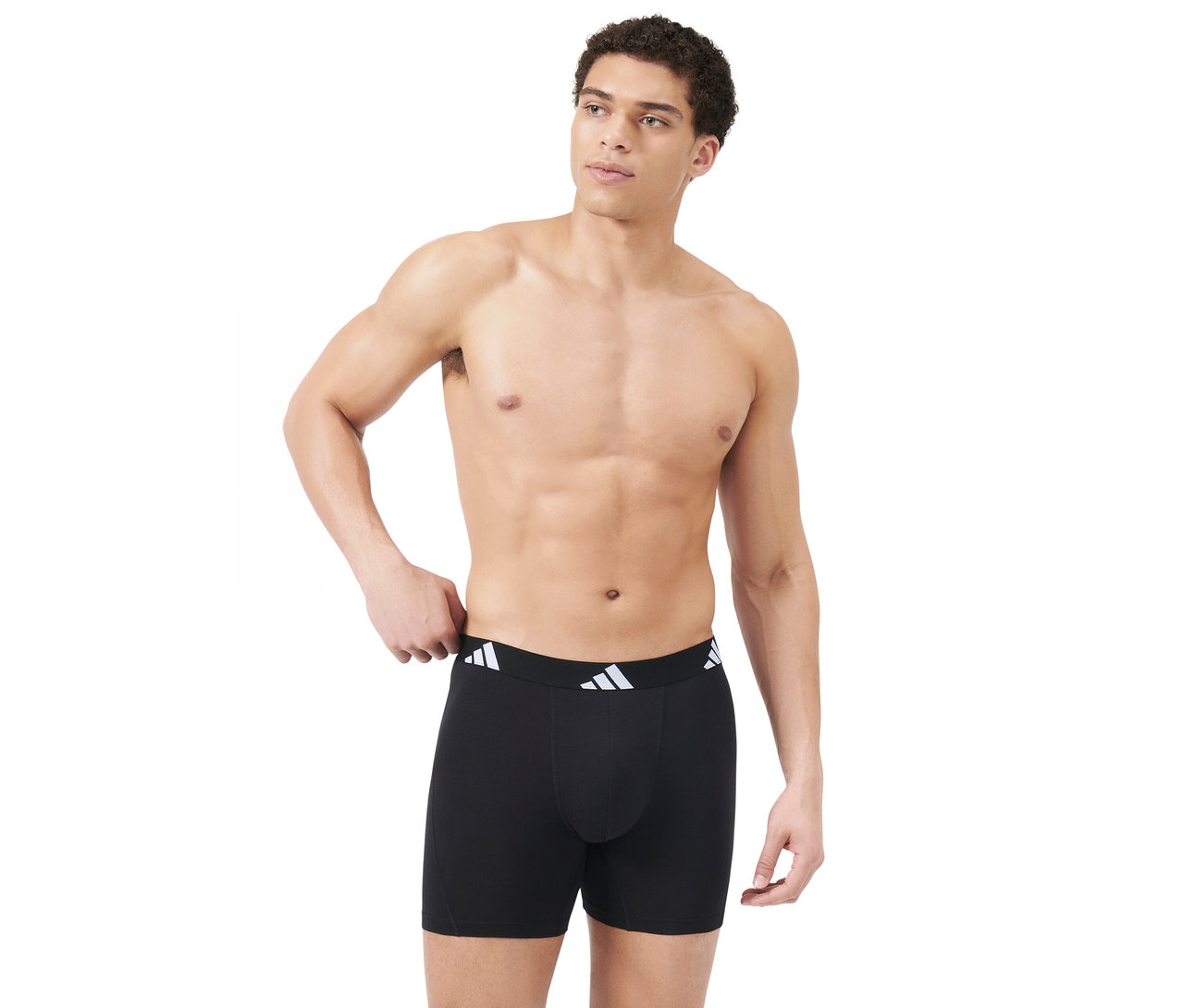Oberkörperfreier Mann trägt schwarze Boxershorts mit weißem adidas Logo-Bund, blickt nach rechts und hält die linke Hand am Bund.