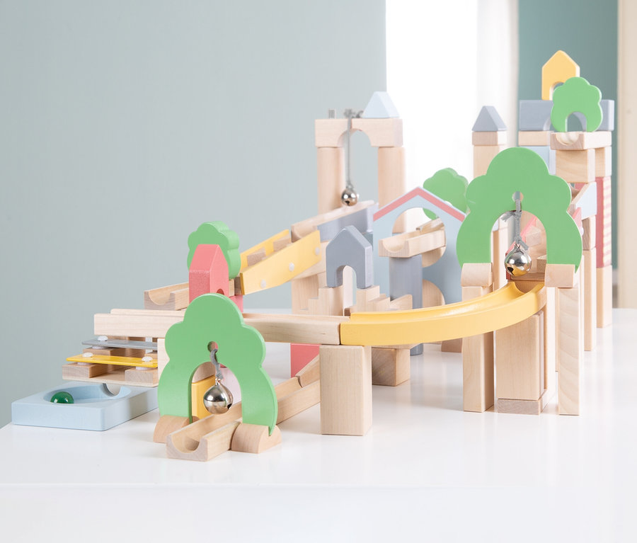 Bunte Holz-Kugelbahn mit gelben, blauen und grünen Bahnen, Glocken und Murmeln auf einer weißen Oberfläche.