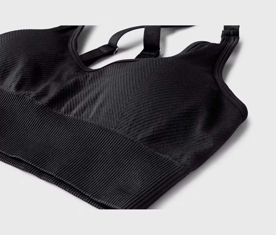 Schwarzer Sport-BH aus geripptem Stoff, mit horizontalen Rippen am Bund und einem Chevron-Muster am Hauptteil. Verstellbare Kreuzträger sind sichtbar.