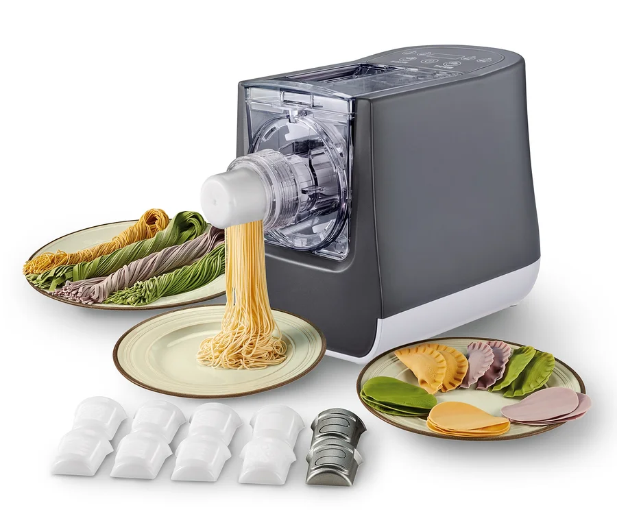 Ein automatischer Pastamaker mit verschiedenen Nudelsorten auf Tellern und Pastaaufsätzen im Vordergrund. Trebs vollautomatische Pastamaschine »99333«.