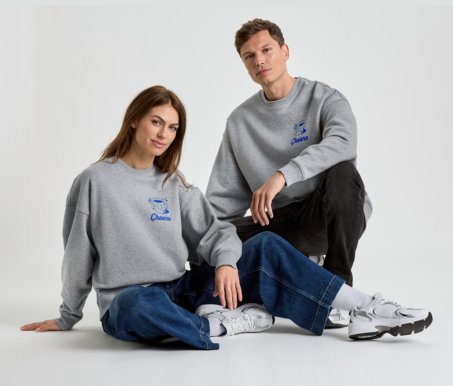 Eine Frau und ein Mann sitzen auf dem Boden und tragen graue Sweatshirts mit der blauen Aufschrift "Cheers".