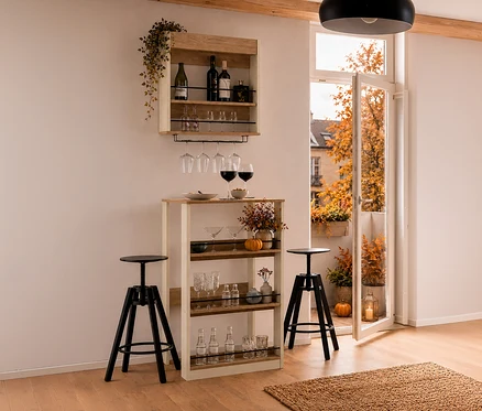 Ein cremebeiges Barregal „Kolari“ hängt über einem cremebeigen Stehtisch „Kolari“ mit Gläsern und Herbstdeko. Zwei schwarze Barhocker stehen davor, daneben ein offener Balkon mit Herbstbäumen.