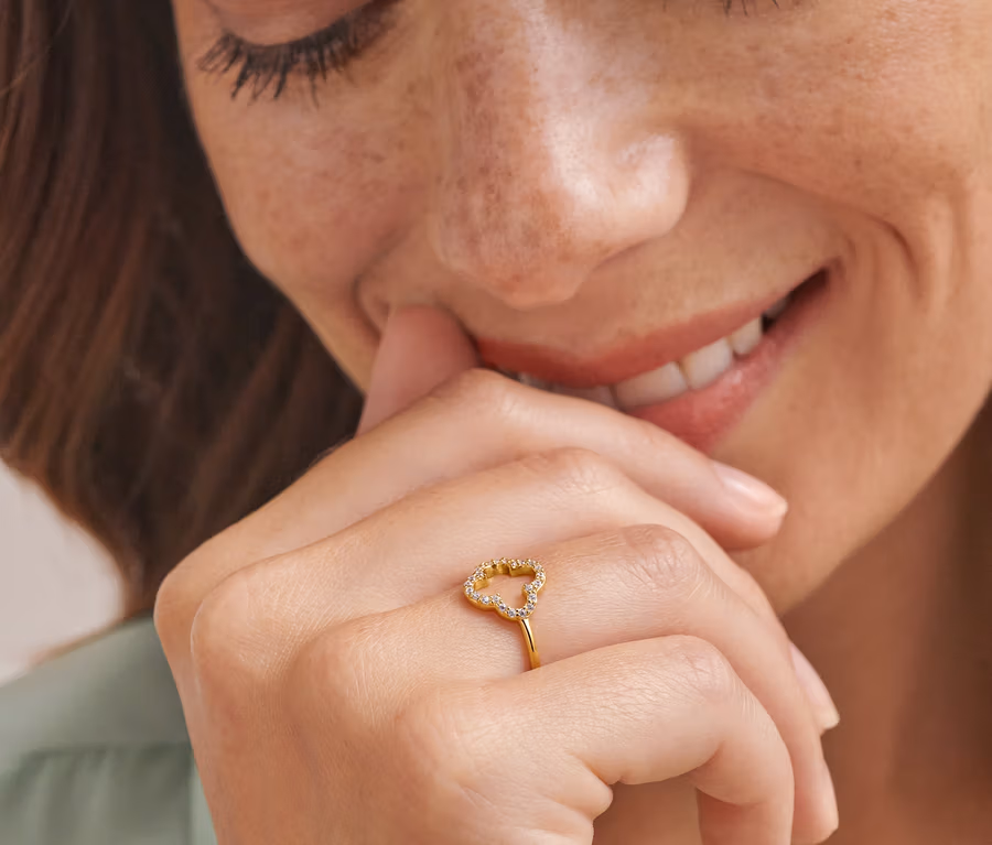Frau lächelt und berührt ihr Gesicht mit einer Hand, die einen Gold Ring Zirkonia Kleeblatt trägt.