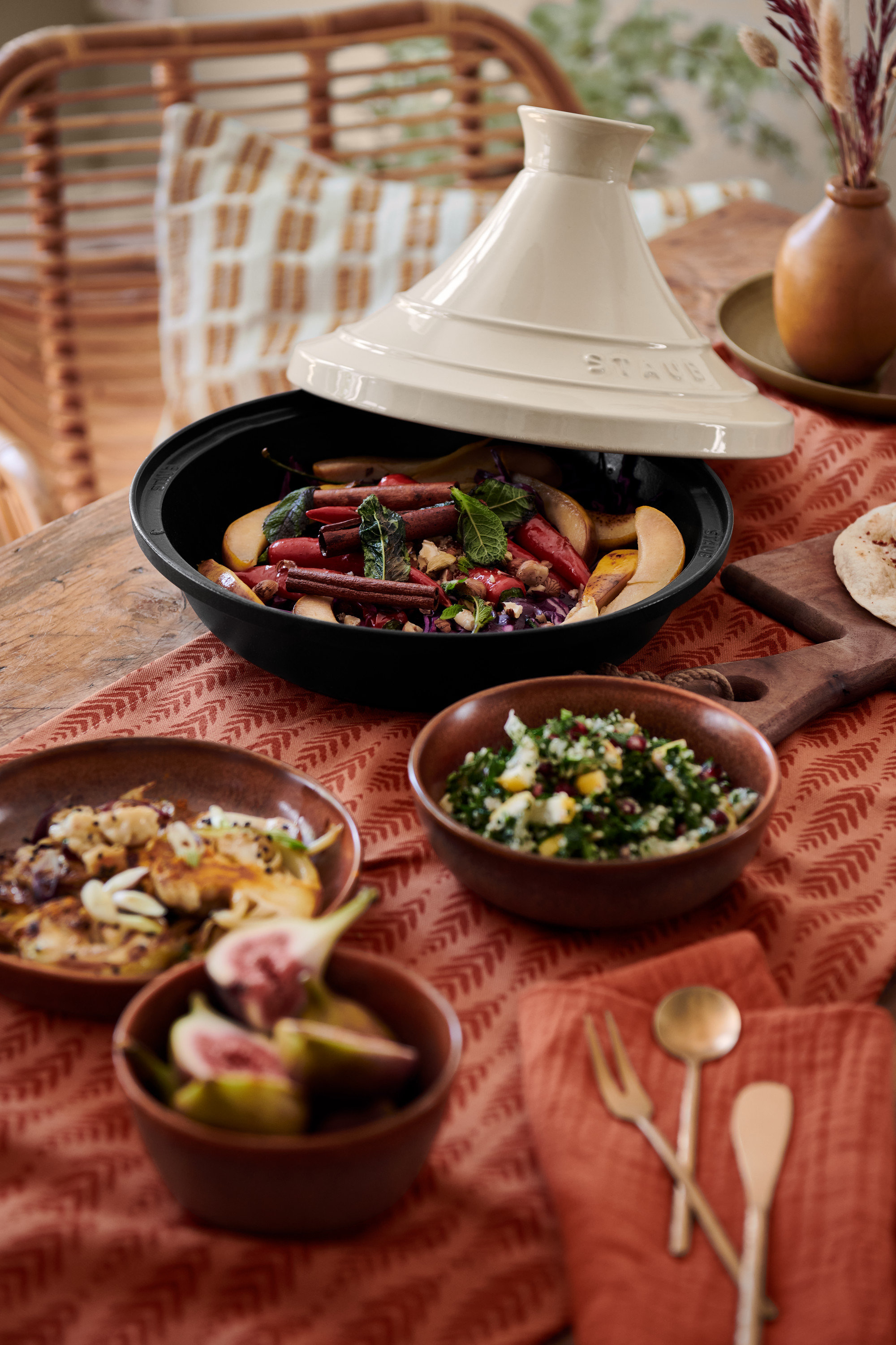 Auf einem Tisch stehen eine Staub-Tajine, 3 Schalen, 2 Dekotabletts, ein 3er-Besteckset und ein Baumwoll-Tischläufer.