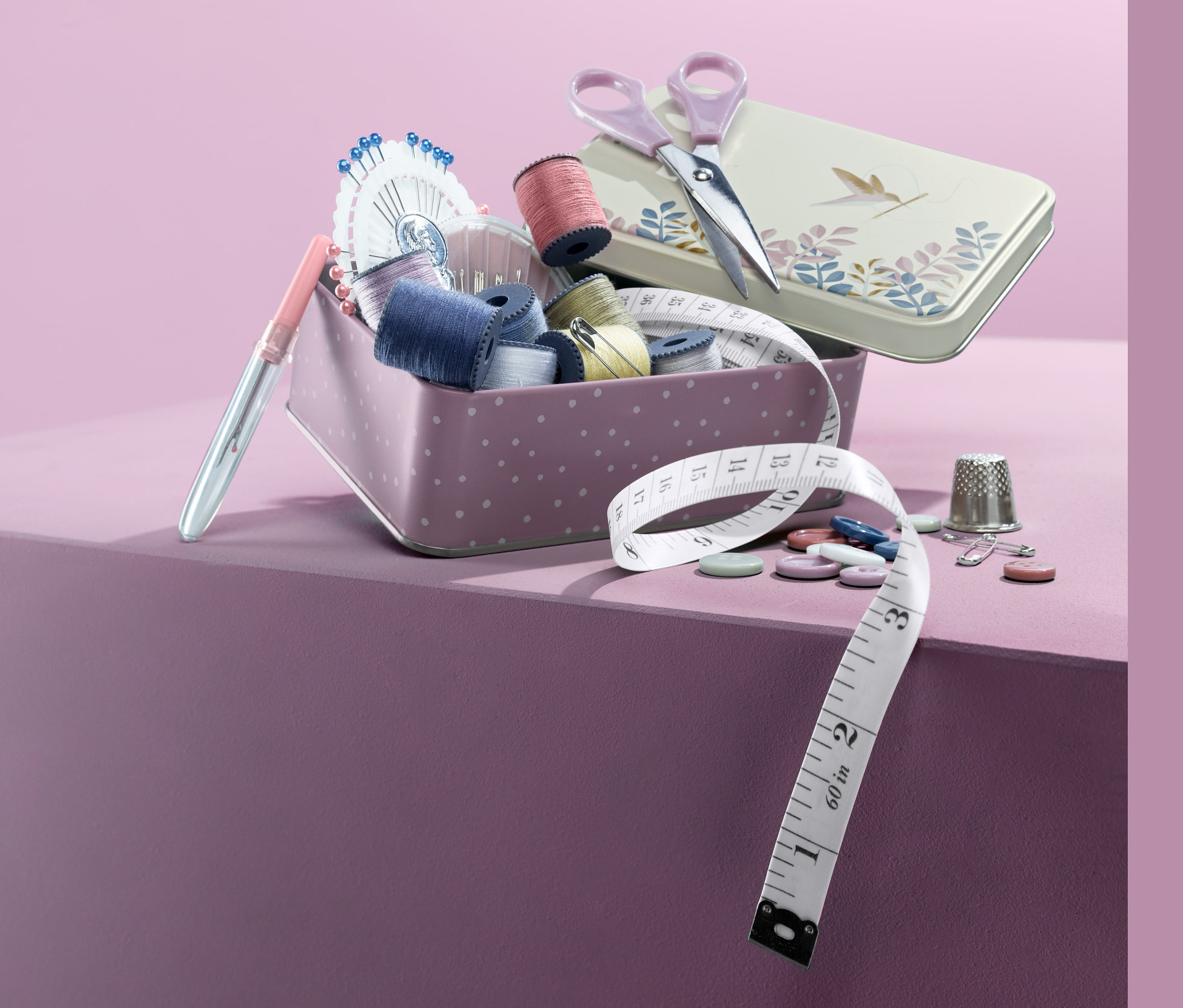 Näh-Set in Metallbox mit Schere, Knöpfen, Nadeln und Maßband auf lila Hintergrund.