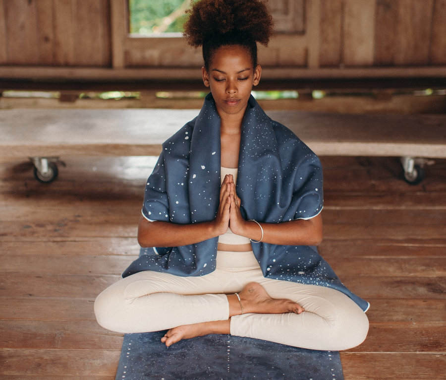 Frau sitzt mit gekreuzten Beinen auf einer Yogamatte mit den Händen in Namasté-Position.