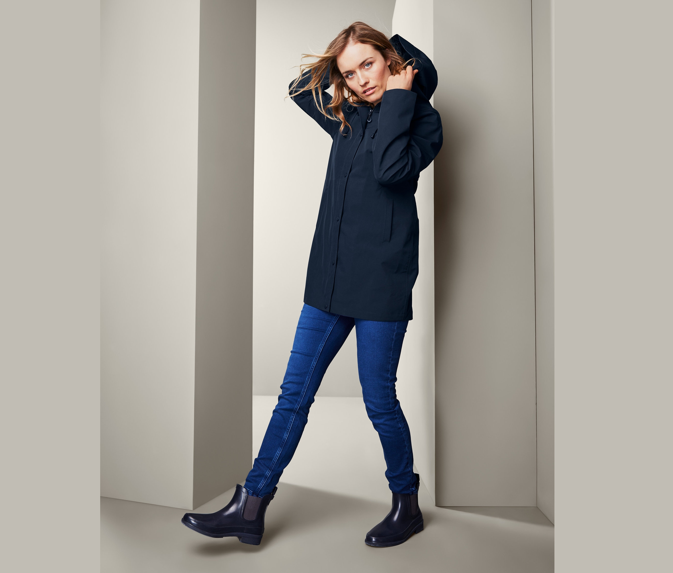 Frau posiert in Hardshell-Regenparka, blauen Jeans und schwarzen Stiefeln.