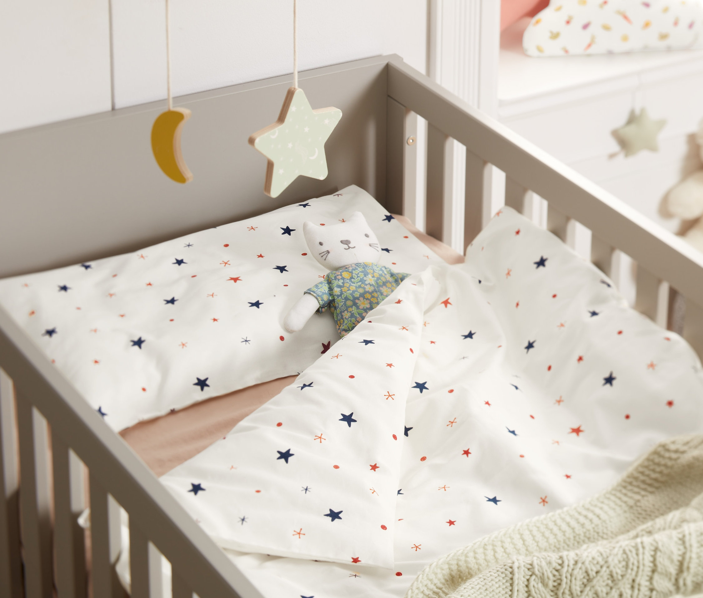 Baby-Bettwäsche mit Sternenmuster und ein Katzenkuscheltier liegen im Kinderbett.