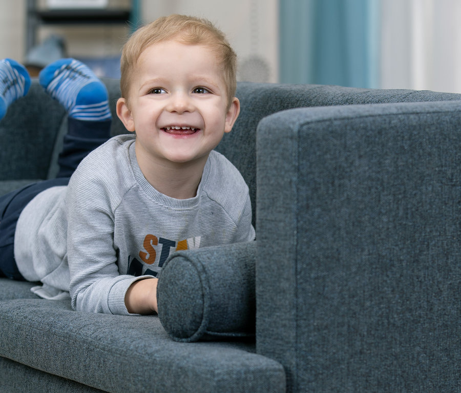 Lächelnder Junge liegt auf blauem Kindersofa »Orion«.