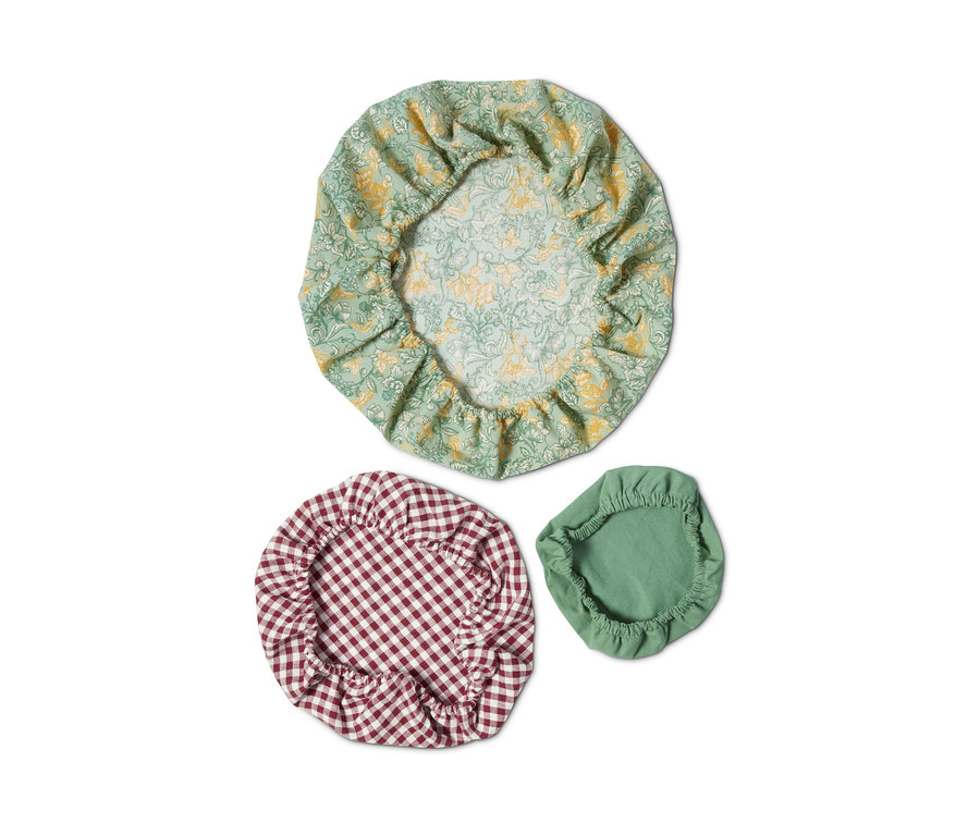 Drei Textil-Deckelhauben: eine mit grünem Blumenmuster, eine mit rotem Karomuster und eine grüne.