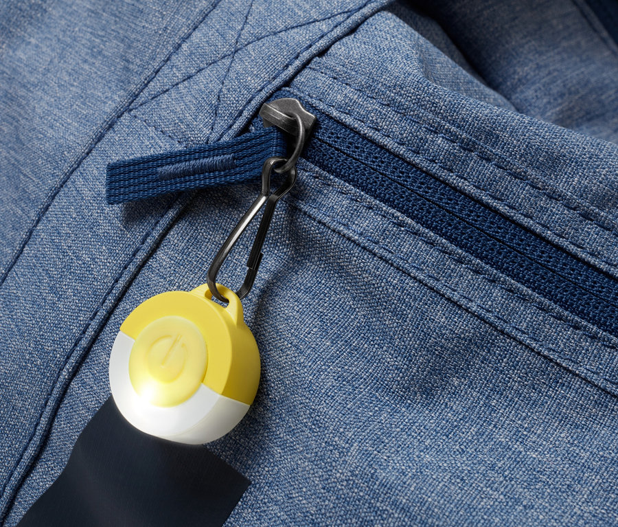 Detailaufnahme einer blauen Stoffjacke mit Reißverschluss und gelb-weißem LED-Anhänger.