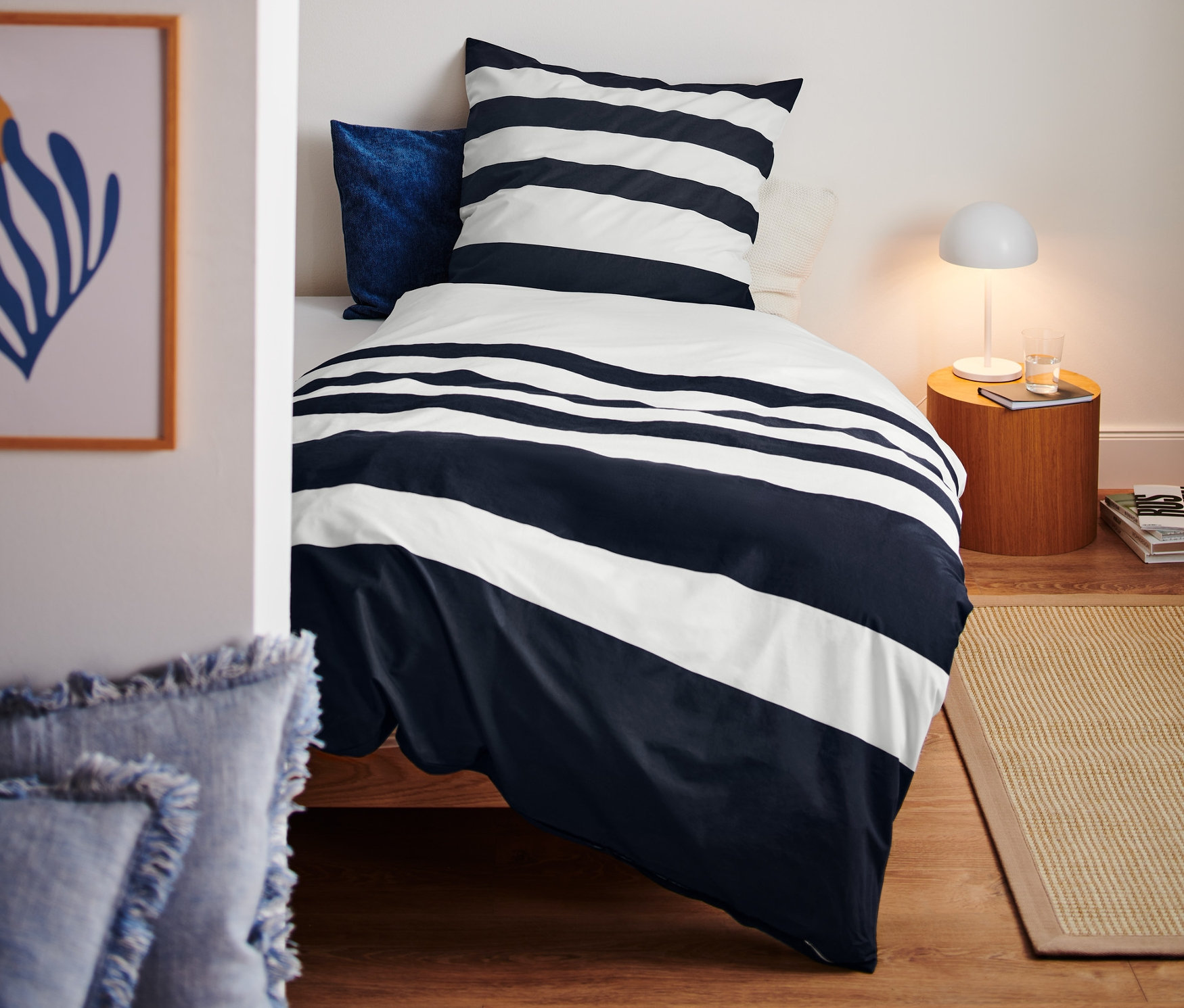 Blick in ein Schlafzimmer mit einem Bett mit Premium-Baumwoll-Bettwäsche mit blau-weißem Streifenmuster.