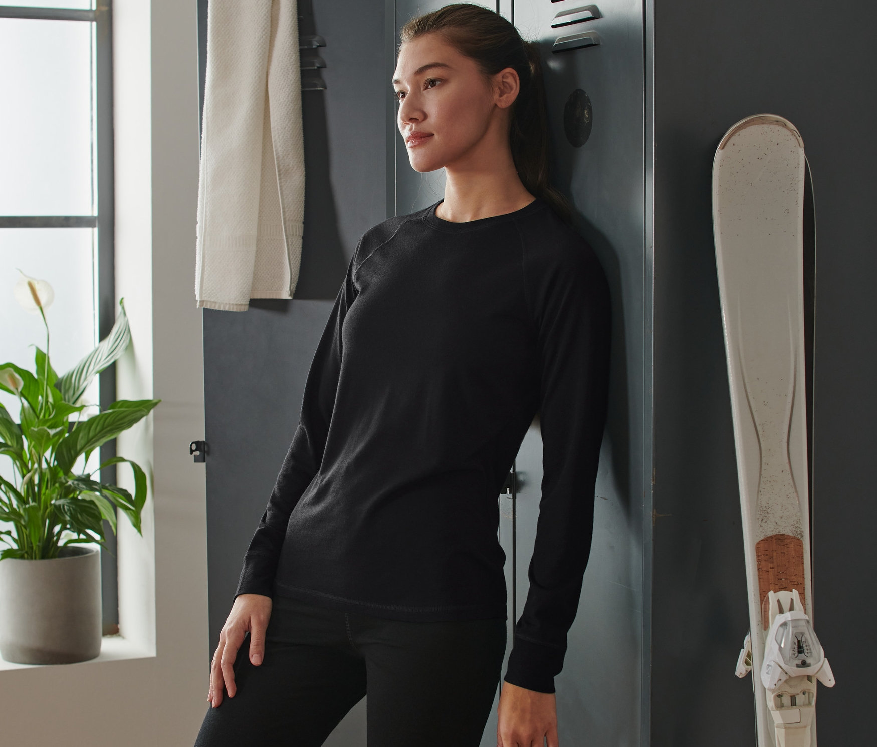 Frau lehnt an Spind und trägt ein schwarzes Funktionsshirt mit Merinowolle.