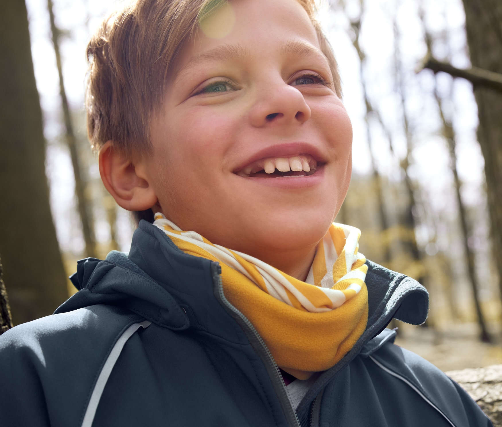 Lächelnder Junge trägt eine Softshell-Jacke und ein Multifunktionstuch.