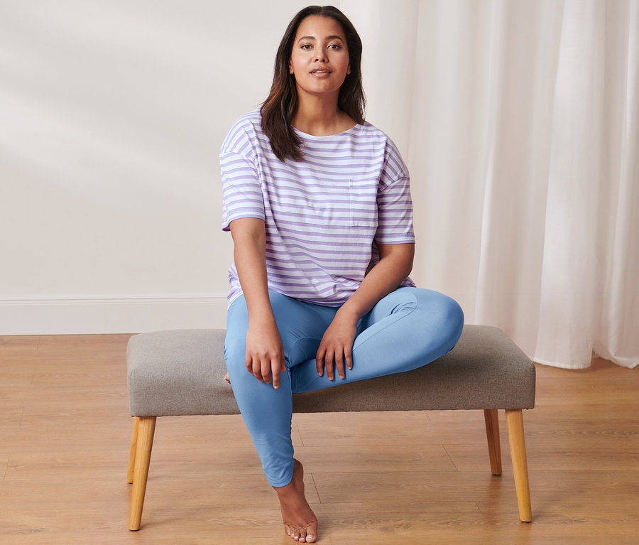 Eine Frau sitzt auf einer Bank und trägt einen Leggings-Pyjama.