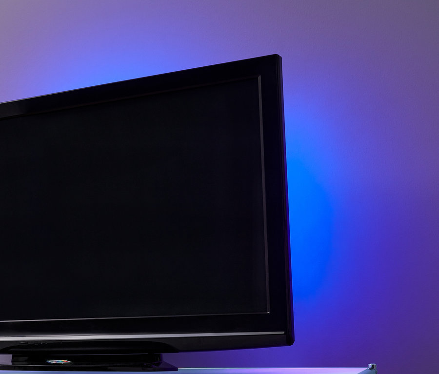 Schwarzer Fernseher mit LED-TV-Hintergrundbeleuchtung an einer Wand mit violett-blauem Licht.