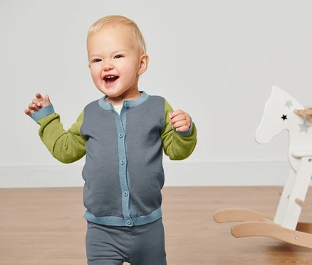 Lächelndes Kind winkt mit den Händen und trägt eine Baby-Strickjacke.